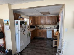 The kitchen features wood cabinetry, a white refrigerator, and a white dishwasher - 