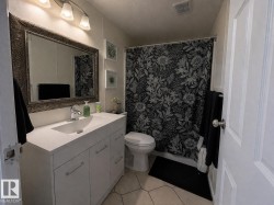 The bathroom features a modern vanity with a white countertop and an integrated sink, complemented by a large framed mirror - 