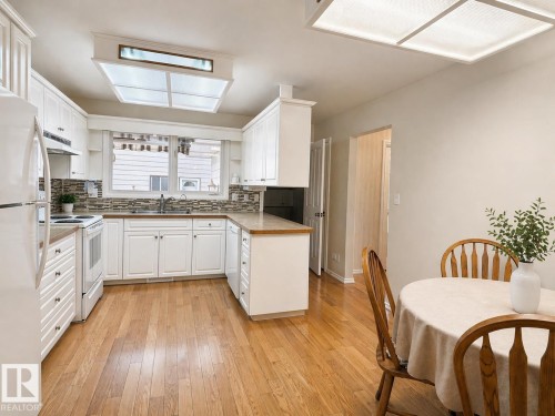 Kitchen featuring white cabinetry, light wood-finish flooring, a mosaic tile backsplash, and a window above the sink - 11139 30 Avenue, Edmonton, AB - Indoor
