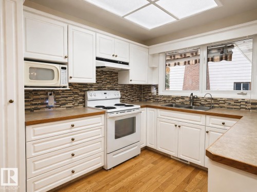 U-shaped kitchen with white cabinetry and wood-finish countertops - 11139 30 Avenue, Edmonton, AB - Indoor Photo Showing Kitchen With Double Sink