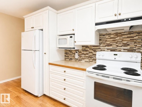 Kitchen featuring white cabinetry with brass hardware, wood-finish flooring, a mosaic tile backsplash, built-in microwave, and white appliances including a refrigerator and electric range - 11139 30 Avenue, Edmonton, AB - Indoor Photo Showing Kitchen