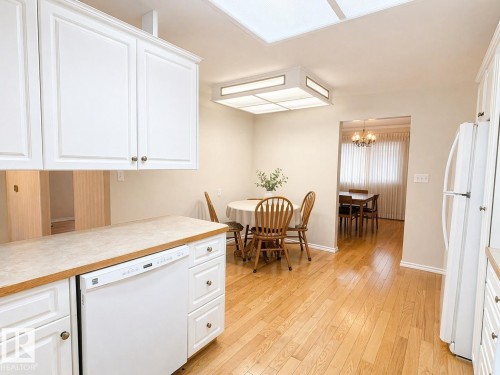 Kitchen area featuring white cabinetry with brass-tone hardware, a white built-in dishwasher, and wood-finish flooring - 11139 30 Avenue, Edmonton, AB - Indoor