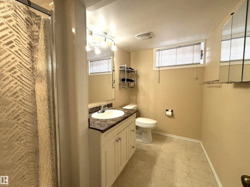 Full bathroom featuring a shower stall with textured glass, a single vanity with a dark countertop and white cabinetry, a white toilet, and tile-finish flooring - 11139 30 Avenue, Edmonton, AB - Indoor Photo Showing Bathroom