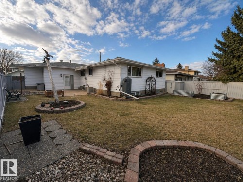 Expansive backyard featuring a central circular garden bed with brick pavers, a concrete patio area, and a white privacy fence - 11139 30 Avenue, Edmonton, AB - Outdoor