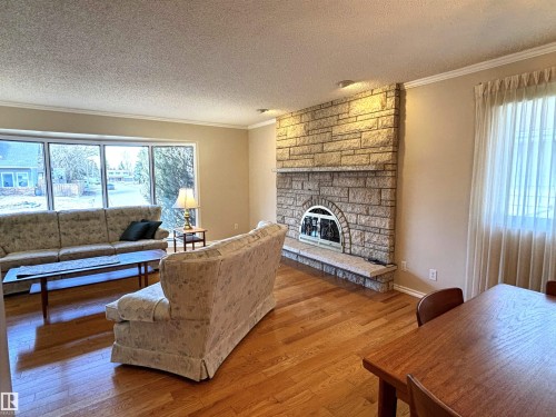 Living area featuring a stone-clad fireplace with a hearth, expansive bay windows, wood-finish flooring, and crown molding - 11139 30 Avenue, Edmonton, AB - Indoor Photo Showing Living Room With Fireplace
