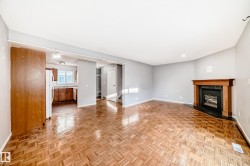 The spacious living area features parquet flooring, a corner fireplace with a wooden mantel, and light grey walls - 