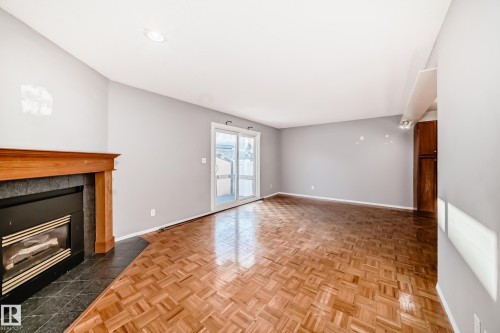 Living area featuring parquet wood flooring, a fireplace with a wood mantel and dark tile surround, and sliding glass doors - 8217 182 Street Nw, Edmonton, AB - Indoor With Fireplace