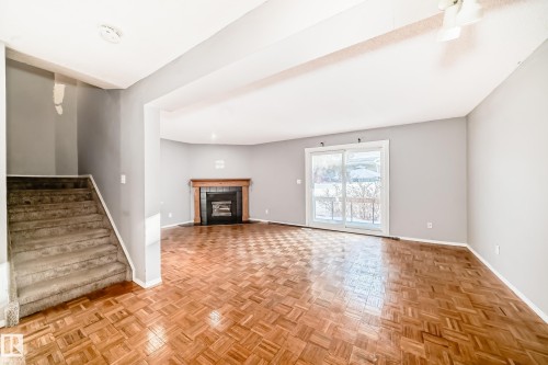Living area featuring parquet wood flooring, a fireplace with a wood mantle and dark tile surround, and a sliding glass door - 8217 182 Street Nw, Edmonton, AB - Indoor With Fireplace