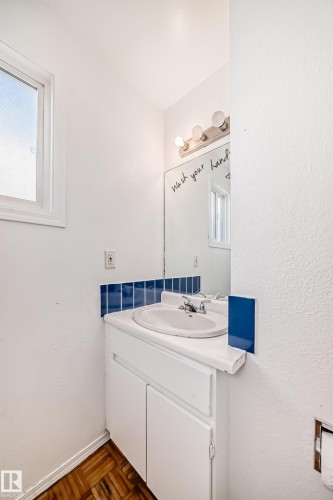 Bathroom featuring a white vanity with an integrated sink, a mirror with a three-light fixture, and blue tiled backsplash - 8217 182 Street Nw, Edmonton, AB - Indoor Photo Showing Bathroom