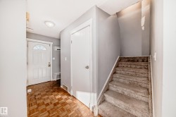 Entryway featuring patterned wood flooring, a white front door with a decorative glass insert, and a carpeted staircase - 