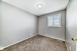 The room features neutral gray walls, brown carpet, and a window with blinds - 