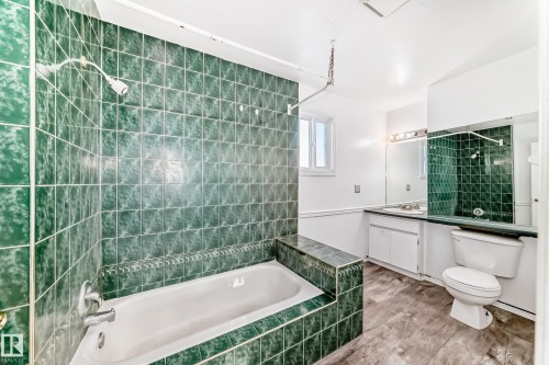 Bathroom featuring a bathtub with green tiled surround, a white toilet, and a vanity with a mirror and overhead lighting - 8217 182 Street Nw, Edmonton, AB - Indoor Photo Showing Bathroom