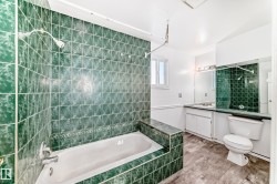 Bathroom featuring a bathtub with green tiled surround, a white toilet, and a vanity with a mirror and overhead lighting - 