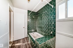 Bathroom featuring a bathtub with green tile surround, a window providing natural light, and wood-look flooring - 