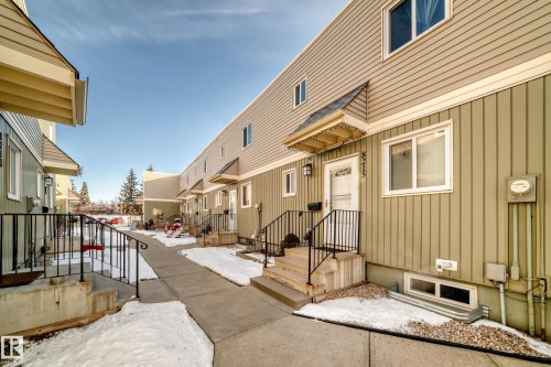 The property features a multi-story exterior with horizontal and vertical siding, a front entry with a small awning, and a window well visible at ground level - 8217 182 Street Nw, Edmonton, AB - Outdoor With Exterior