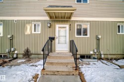 The property features a front entrance with concrete steps and black metal railings, leading to a white door with a storm door - 