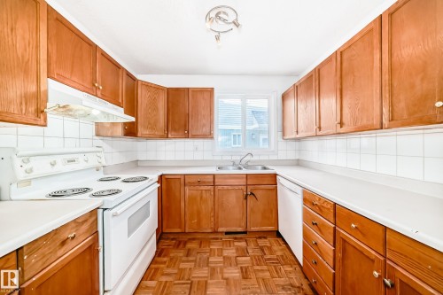 The kitchen features light wood cabinetry, white countertops, white appliances, and a window above the double sink - 8217 182 Street Nw, Edmonton, AB - Indoor Photo Showing Kitchen With Double Sink