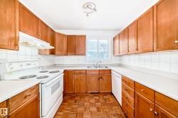 The kitchen features light wood cabinetry, white countertops, white appliances, and a window above the double sink - 