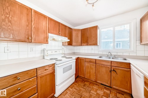 The kitchen features wood cabinetry, white countertops, a white tile backsplash, and a double basin sink - 8217 182 Street Nw, Edmonton, AB - Indoor Photo Showing Kitchen With Double Sink