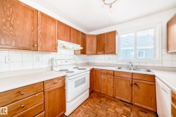The kitchen features wood cabinetry, white countertops, a white tile backsplash, and a double basin sink - 