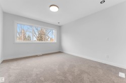 Spacious room featuring a large horizontal window, light neutral carpet, white walls, and recessed ceiling lighting complemented by a central flush mount fixture - 