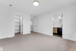 Spacious room with plush carpeting, two built-in closet systems with shelving, a contemporary flush-mount ceiling light, and access to a bathroom featuring a modern vanity with dual sinks, an oval mirror, and dark-toned flooring - 