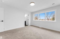Spacious room featuring light gray carpeting, crisp white walls, a large three-panel window, a flush-mount ceiling light, and a modern door with black hardware - 