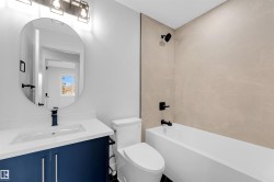 Modern bathroom featuring a deep blue vanity with white countertop, oval mirror, and a built-in bathtub with light-toned tile surround - 
