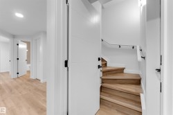 Wood-finish flooring throughout, bright white walls, modern panel doors with matte black hardware, and a staircase with a contrasting white handrail - 