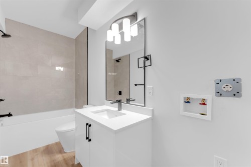 Bathroom featuring a white vanity with integrated sink, a rectangular mirror with dark trim, and a bathtub with light-toned tiled surround - 7934 77 Avenue, Edmonton, AB - Indoor Photo Showing Bathroom