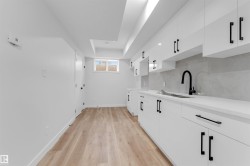 Contemporary kitchen space featuring white cabinetry with matte black hardware, light-toned wood-finish flooring, and a window for natural light - 