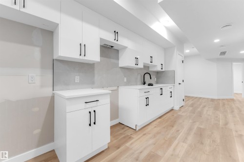 Modern kitchen space featuring white cabinetry with matte black hardware, a black gooseneck faucet, light wood-finish flooring, and recessed ceiling lighting - 7934 77 Avenue, Edmonton, AB - Indoor Photo Showing Kitchen