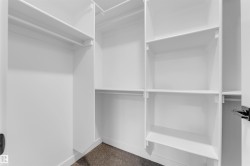 Walk-in closet featuring white built-in shelving, multiple hanging rods, and dark carpet flooring - 