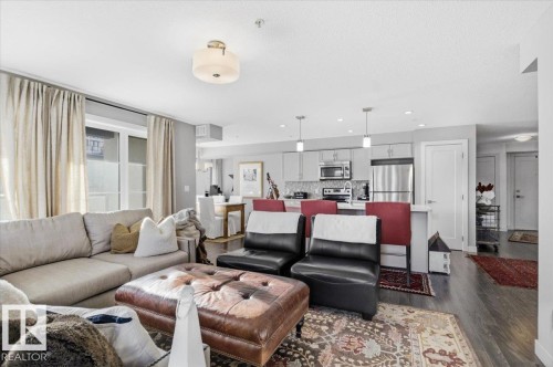 Open concept living space featuring dark wood flooring, light neutral walls, and a contemporary light fixture - 211 5029 Edgemont Boulevard, Edmonton, AB - Indoor Photo Showing Living Room