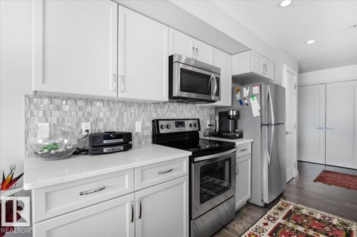The kitchen features white cabinetry, stainless steel appliances including a microwave and range, and a tiled backsplash - 211 5029 Edgemont Boulevard, Edmonton, AB - Indoor Photo Showing Kitchen