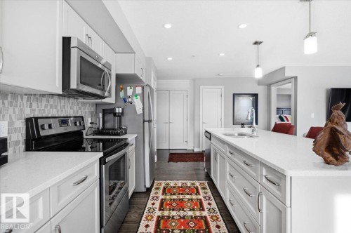 The kitchen features white cabinetry, stainless steel appliances, and a mosaic tile backsplash - 211 5029 Edgemont Boulevard, Edmonton, AB - Indoor Photo Showing Kitchen With Upgraded Kitchen
