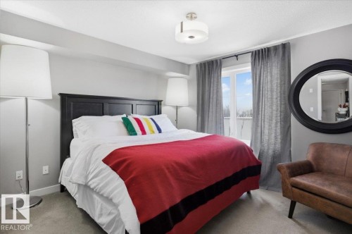 Bedroom featuring a large window, a dark wood headboard, and light grey walls - 211 5029 Edgemont Boulevard, Edmonton, AB - Indoor Photo Showing Bedroom