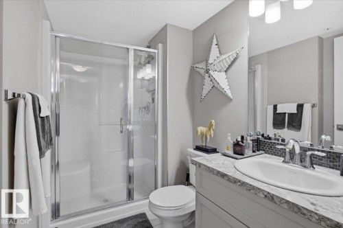 Bathroom featuring a shower with a sliding glass door, a vanity with a white basin sink, and a mirrored wall - 211 5029 Edgemont Boulevard, Edmonton, AB - Indoor Photo Showing Bathroom