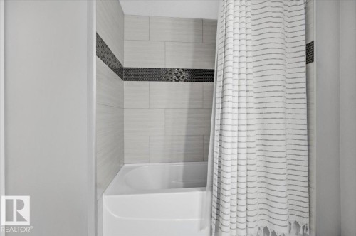 Bathroom featuring a tub and shower combination with light-colored tile surround and a decorative mosaic tile accent band - 211 5029 Edgemont Boulevard, Edmonton, AB - Indoor Photo Showing Bathroom