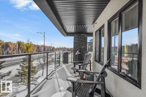The property features a balcony with a glass railing, offering views of the surrounding trees and a road - 211 5029 Edgemont Boulevard, Edmonton, AB - Outdoor With Balcony With Exterior