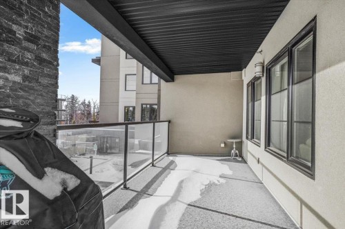 This property features an exterior balcony with a glass railing and a stone-clad wall - 211 5029 Edgemont Boulevard, Edmonton, AB - Outdoor With Balcony With Exterior