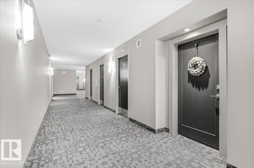Hallway featuring wall sconces, ceiling-mounted lighting, and carpeted flooring - 211 5029 Edgemont Boulevard, Edmonton, AB - Indoor Photo Showing Other Room