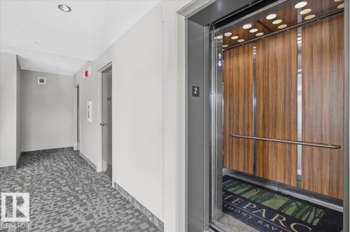 The property features an elevator with wood paneling and a stainless steel handrail, complementing the hallway's recessed lighting and patterned carpet - 211 5029 Edgemont Boulevard, Edmonton, AB - Indoor Photo Showing Other Room
