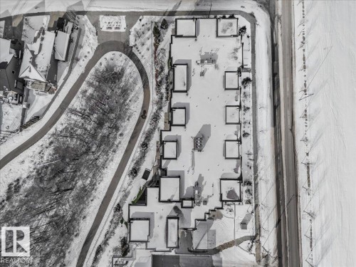 Aerial view of the property and its surrounding area, featuring a paved road, a winding pathway, and rows of structures with snowy rooftops - 211 5029 Edgemont Boulevard, Edmonton, AB - 