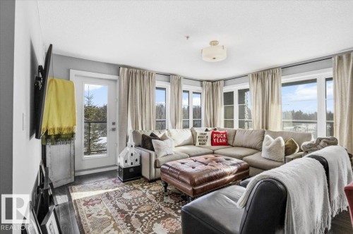 This bright living space features large windows, a glass-paned door, and wood flooring - 211 5029 Edgemont Boulevard, Edmonton, AB - Indoor Photo Showing Living Room