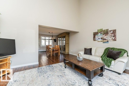 Living area featuring high ceilings, wood-finish flooring, and a broad arched entryway into the dining space - 1727 65 Street, Edmonton, AB - Indoor Photo Showing Living Room
