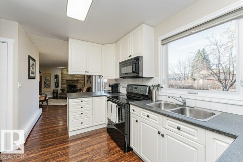 Kitchen featuring white cabinetry, dark countertops, a double stainless steel sink, black appliances, and wood-finish flooring - 1727 65 Street, Edmonton, AB - Indoor Photo Showing Kitchen With Double Sink