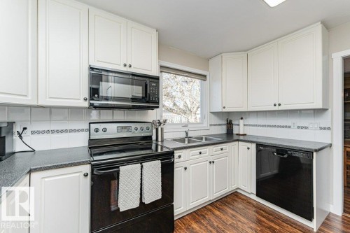 Kitchen featuring white cabinetry, dark countertops, a double basin sink, a black over-the-range microwave, and dark wood-finish flooring - 1727 65 Street, Edmonton, AB - Indoor Photo Showing Kitchen With Double Sink
