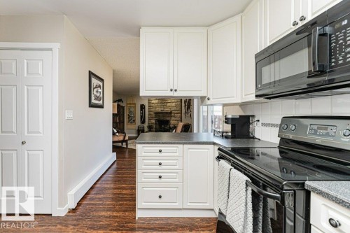Kitchen featuring white cabinetry, dark speckled countertops, white tile backsplash, and wood-finish flooring - 1727 65 Street, Edmonton, AB - Indoor Photo Showing Kitchen