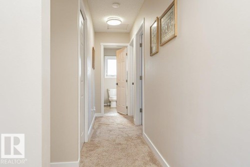 Hallway with neutral wall paint, light-colored carpet flooring, recessed ceiling light, white trim, and a visible doorway leading to a bathroom with a window - 1727 65 Street, Edmonton, AB - Indoor Photo Showing Other Room